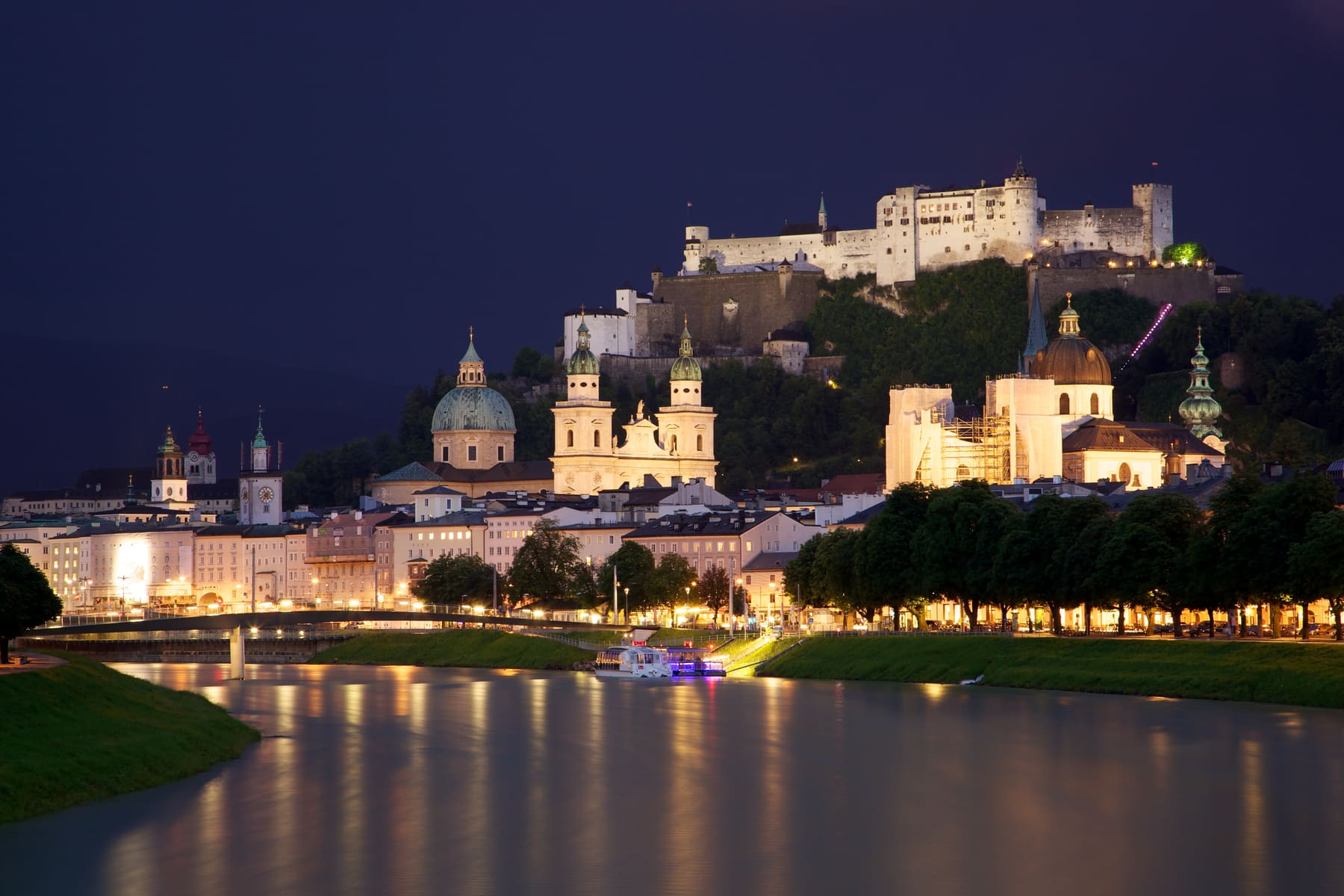 Salzburg old town and Hohensalzburg Fortress lit up at dusk, reflected in the Salzach river