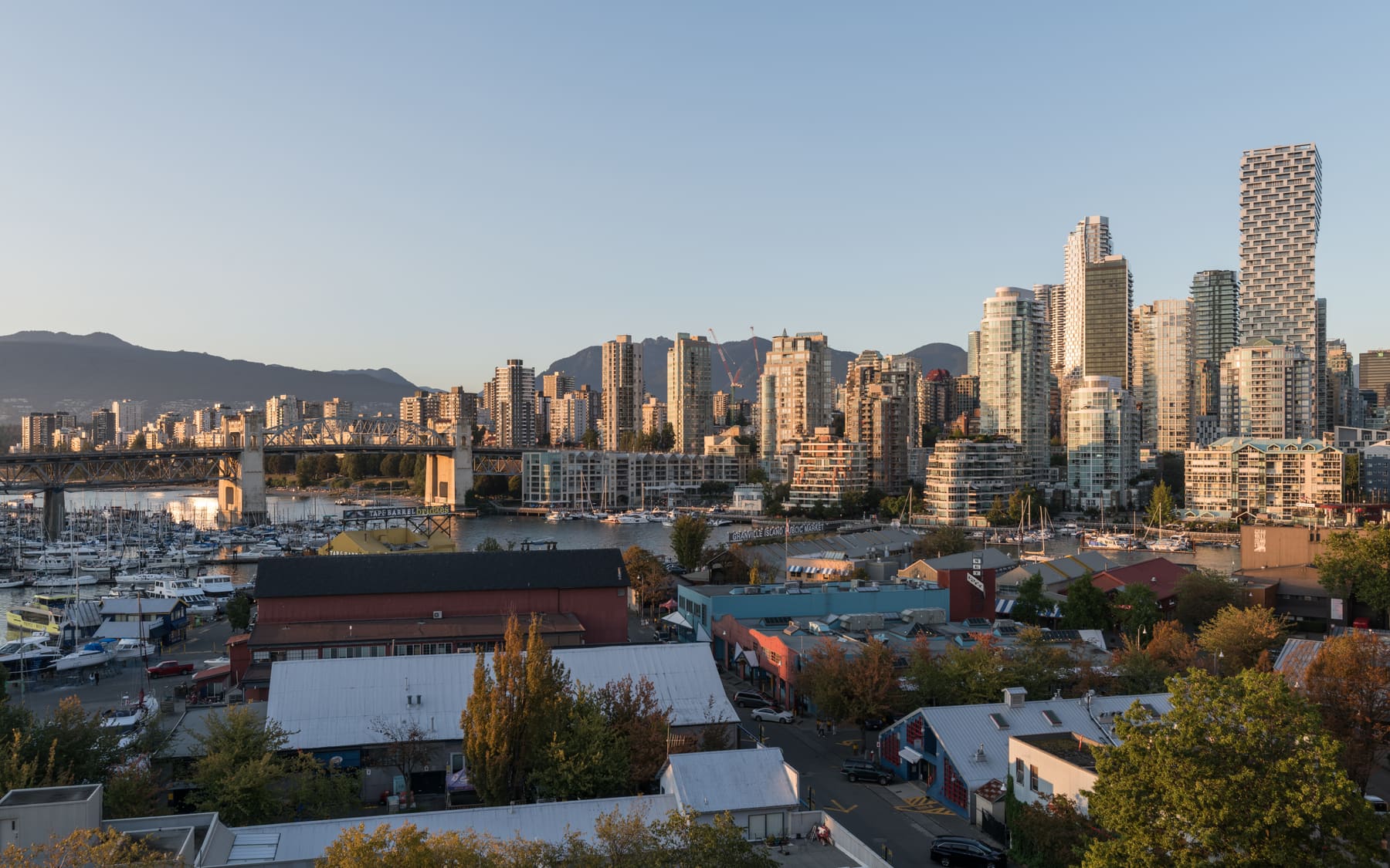 Downtown Vancouver high-rise towers beyond a marina and Granville Island rooftops, with mountains in the background