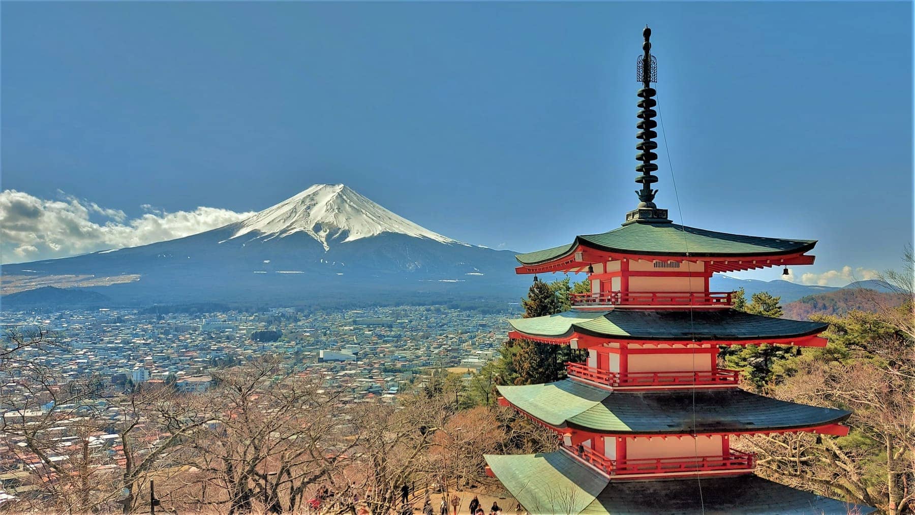 The red Chureito Pagoda in the foreground with a snow-capped Mount Fuji and the town of Fujiyoshida in the distance