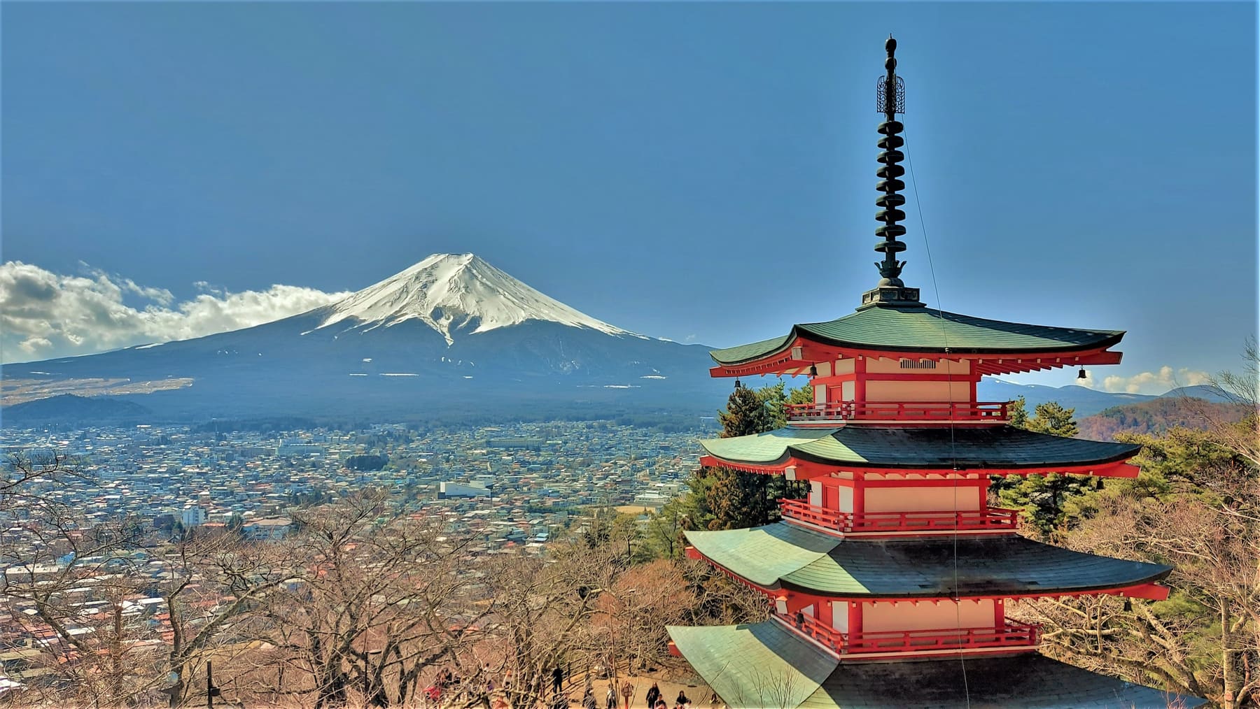 The red Chureito Pagoda in the foreground with a snow-capped Mount Fuji and the town of Fujiyoshida in the distance