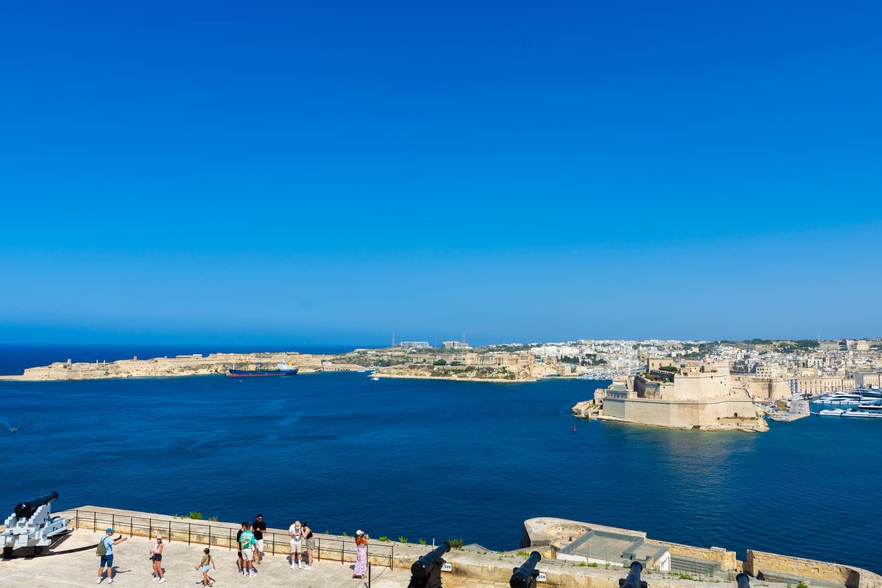 Blue waters of the Grand Harbour with a fortified peninsula and waterfront buildings, seen from a terrace in Valletta