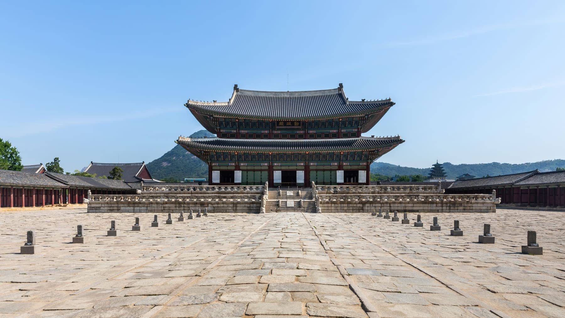 Front view of Geunjeongjeon, the throne hall of Gyeongbokgung Palace, across a stone courtyard under a blue sky in Seoul