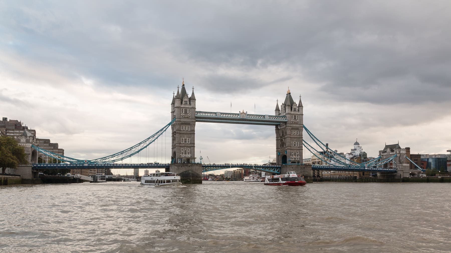 Tower Bridge crossing the River Thames in London, photographed from the river under a cloudy sky